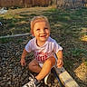 toddler, child, smiling, sitting, rocks, backyard, sunlight, grass, fence, sneakers, clothing, happy, outdoor, person, nature, wood, daylight, casual, cute, playing