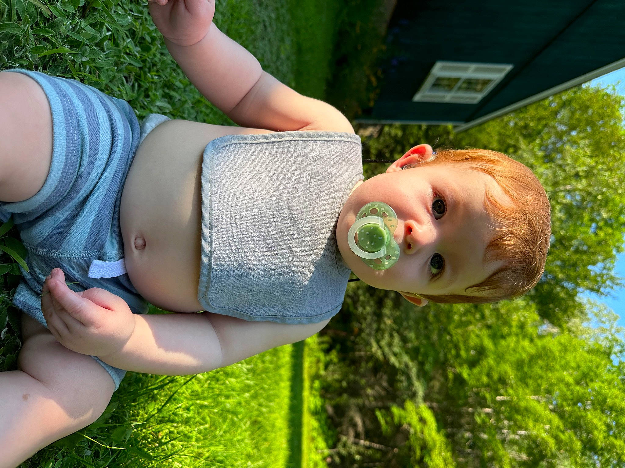 Axl is registered to the contest to win money with this photo: child, facial_expression, gesture, grass, grass_family, green, happy, human_leg, knee, leisure, people_in_nature, person, plant, sky, smile, thigh, toddler, tree, water, window