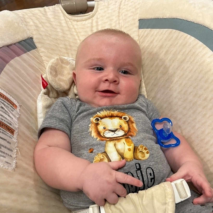Oppie is registered to the contest to win money with this photo: baby, baby_seat, child, closeup, clothing, comfort, cushion, cute, happy, human, indoor, infant, lion_print, onesie, pacifier, portrait, seatbelt, smile, wooden_floor, young