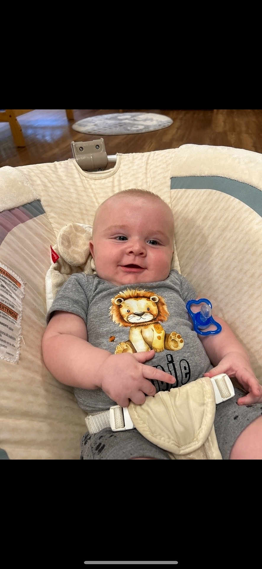 Oppie is registered to the contest to win money with this photo: baby, infant, smile, pacifier, onesie, lion_print, baby_seat, cushion, indoor, wooden_floor, happy, child, cute, young, clothing, seatbelt, human, portrait, closeup, comfort