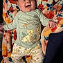 baby, smiling, pajamas, blanket, floral_pattern, cartoon_characters, infant, clothing, happy, face, lying_down, cute, child, soft_texture, indoors, colorful, cozy, toddler, expression, sleepwear