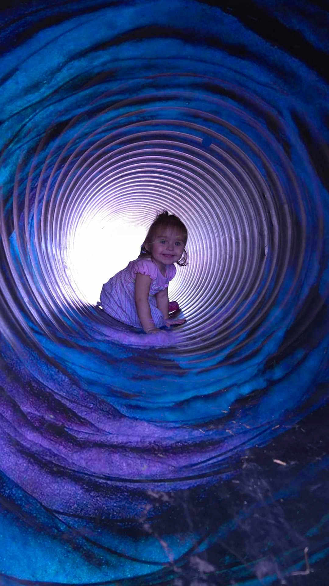Freya joined the competition — help win amazing prizes! toddler, child, girl, tunnel, crawl, purple, blue, spiral, playground, smile, dress, light, cylindrical, fun, outdoor, happy, curly_hair, play, colorful, young_child