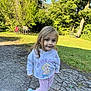 child, girl, hoodie, princess, blue_shoes, outdoor, grass, trees, sunny, pavement, smile, playful, nature, casual_clothing, young_child, happy, daylight, greenery, pants, young_girl
