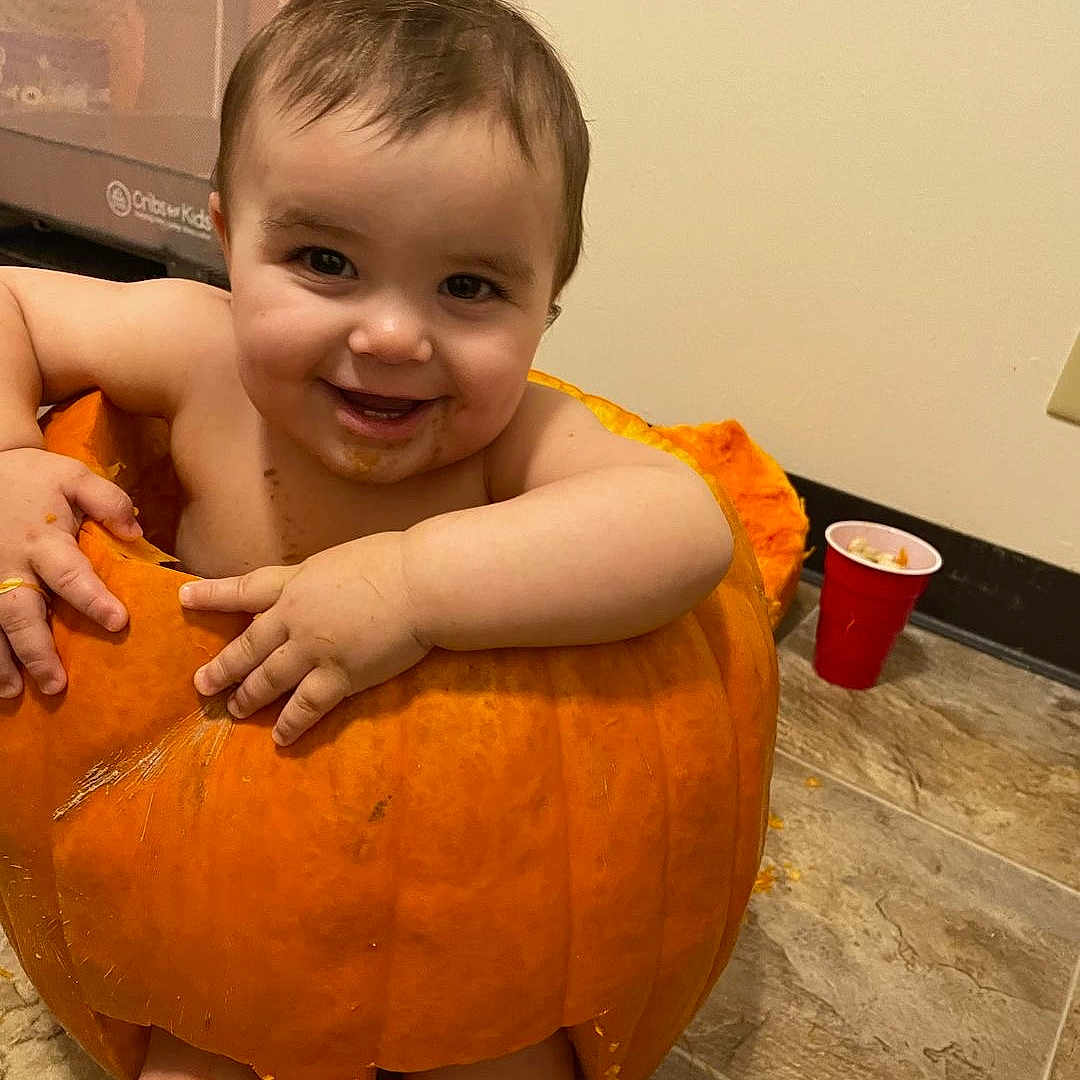 Vaeh joined the competition — help win amazing prizes! baby, child, cute, face, floor, food, fun, halloween, hands, happy, indoor, legs, messy, mouth, orange, person, playful, pumpkin, skin, smiling