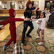 Anniyah is registered to the contest to win money with this photo: adult, boots, carpet, casual_clothing, child, children, colorful_pants, costume, event, fun, group, indoor, patterned_carpet, people, playful, posing, red_hoodie, room, smiling, superhero