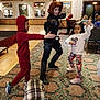 adult, boots, carpet, casual_clothing, child, children, colorful_pants, costume, event, fun, group, indoor, patterned_carpet, people, playful, posing, red_hoodie, room, smiling, superhero