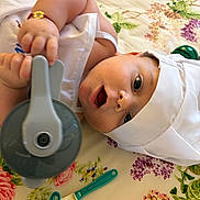 Ayaan participe au concours pour gagner de l'argent avec cette photo : baby, infant, chef_hat, white_clothing, kitchen_utensils, toy, playing, lying_down, floral_pattern, curious_expression, hand, face, indoors, cute, child, apron, cooking_theme, colorful, soft_lighting, small_object