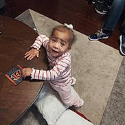 Rumanni is registered to the contest to win money with this photo: toddler, child, table, wooden_table, striped_shirt, pink_pants, remote_control, bowl, nuts, carpet, sneakers, living_room, person, floor, toy, curly_hair, white_bow, indoor, cushion, blur