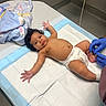 Azorie is registered to the contest to win money with this photo: baby, infant, diaper, medical_table, blanket, gloves, bandage, hospital, clinic, person, child, skin, arm, leg, foot, head, curly_hair, expression, indoor, healthcare