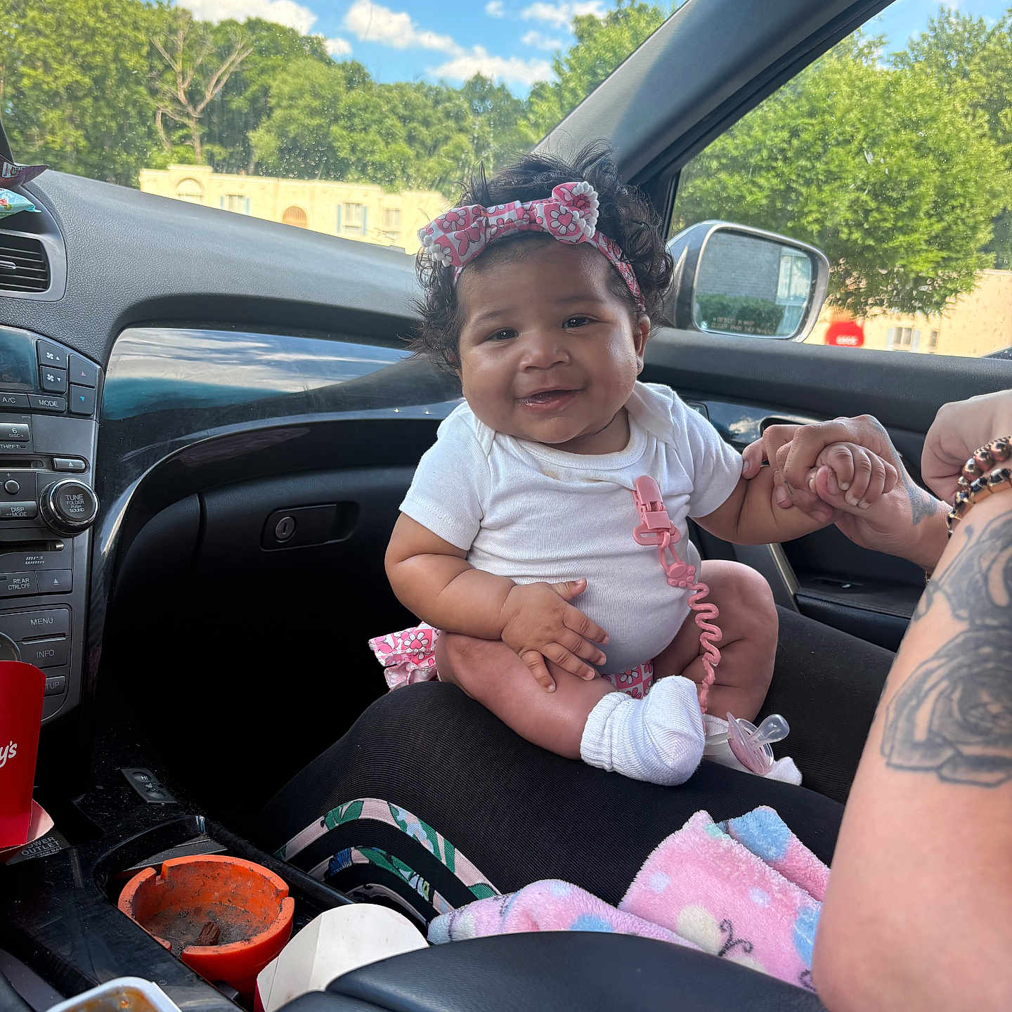 Azorie joined the competition — help win amazing prizes! baby, infant, car_interior, child, smiling, headband, white_clothing, hand_holding, person, seat, window, trees, daytime, sunny, clothing_accessory, tattoo, food_container, car_dashboard, seatbelt, blanket