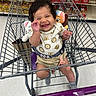 baby, shopping_cart, grocery_store, bread, smiling, child, curly_hair, clothing, toy, socks, person, happy, infant, seatbelt, retail, aisle, floor, hand, cute, indoor