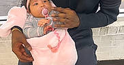 Azorie is registered to the contest to win money with this photo: baby, infant, child, man, holding, indoor, window, pacifier, pink_blanket, headband, seated, floor_tiles, black_clothing, afro_hair, affection, parent_child, love, care, portrait, people