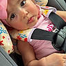 baby, child, car_seat, pink_bow, flower_pattern, seatbelt, infant, cute, portrait, indoors, car, sitting, clothing, headwear, face, hand, expression, child_seat, toddler, safety