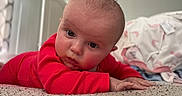 Nightlynn is registered to the contest to win money with this photo: baby, bedding, bedroom, carpet, child, close_up, curious, eyes, face, home, indoor, infant, lying_down, natural_light, photography, portrait, red_clothing, sitting_room, smiling, tummy_time