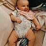 baby, barefoot, bed, bib, blanket, child, closeup, cozy, dog_paw, family, floral_outfit, happy, home, indoors, infant, lying_down, onesie, pillow, portrait, smiling