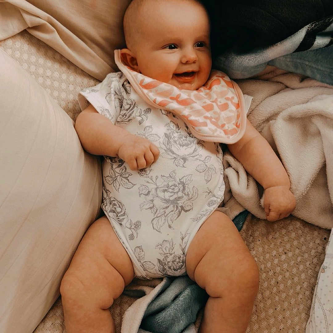 Nightlynn joined the competition — help win amazing prizes! baby, barefoot, bed, bib, blanket, child, closeup, cozy, dog_paw, family, floral_outfit, happy, home, indoors, infant, lying_down, onesie, pillow, portrait, smiling