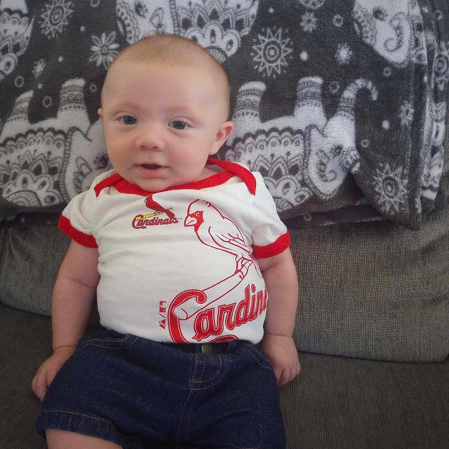 Zander is registered to the contest to win money with this photo: baby, child, infant, portrait, sitting, couch, blanket, baseball, cardinals, sports_fan, clothing, shirt, shorts, denim, face, eyes, smiling, indoors, furniture, photography