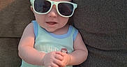 Zander is registered to the contest to win money with this photo: baby, infant, child, sunglasses, couch, sofa, seated, portrait, indoor, home, smiling, face, hands, clothing, romper, mint_green, eyewear, cushions, furniture, cute