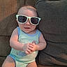 baby, infant, child, sunglasses, couch, sofa, seated, portrait, indoor, home, smiling, face, hands, clothing, romper, mint_green, eyewear, cushions, furniture, cute