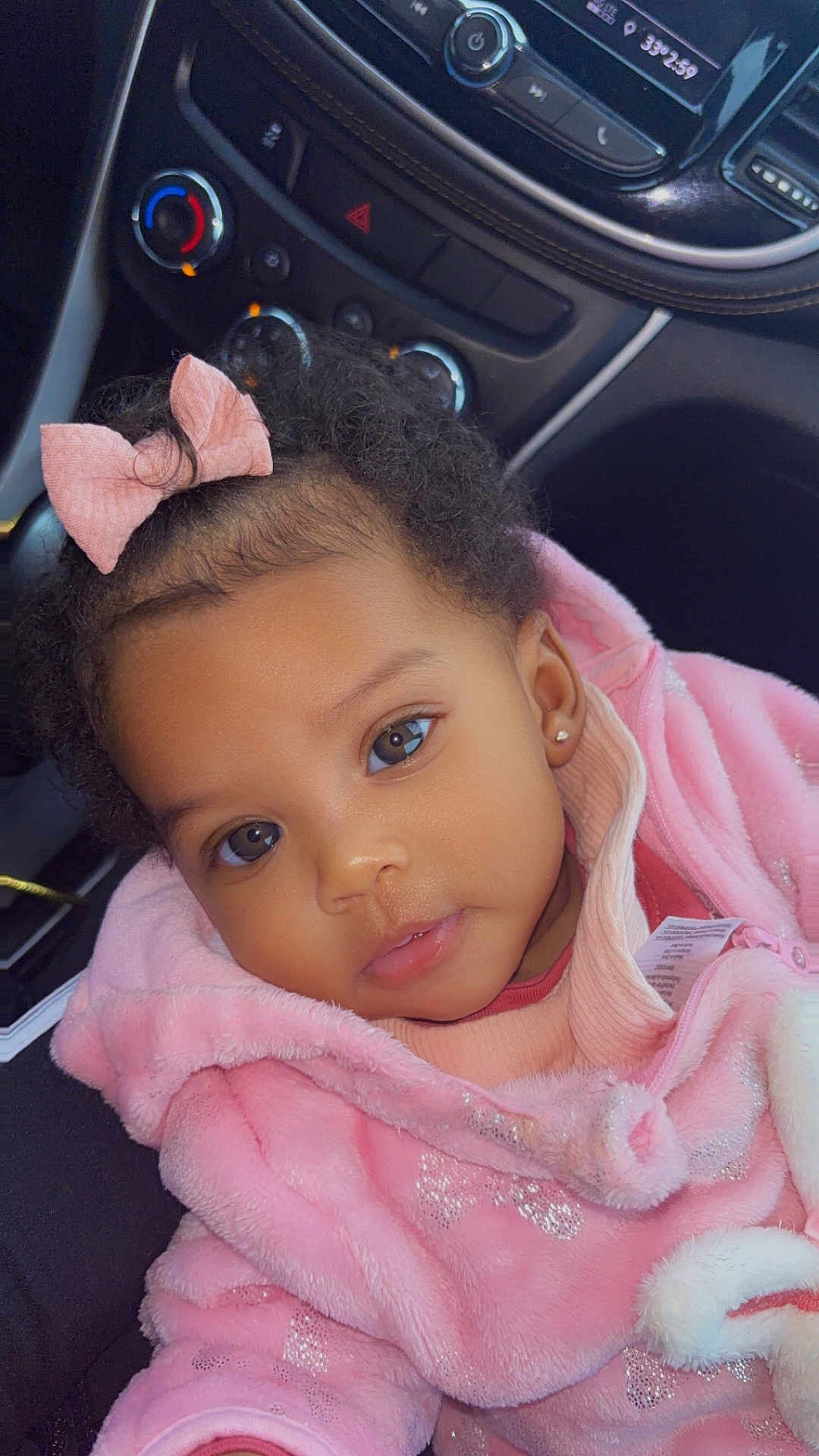 Cyamei is registered to the contest to win money with this photo: toddler, child, pink_jacket, bow, curly_hair, face, ears, eyes, car_interior, dashboard, clothing, cute, portrait, baby, earrings, seat, seatbelt, warm_clothing, indoors, person
