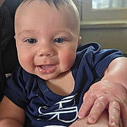 Noah is registered to the contest to win money with this photo: baby, child, smiling, face, hand, blue_shirt, indoor, window, skin, person, portrait, cute, young_child, light, expression, infant, close_up, happy, natural_light, human