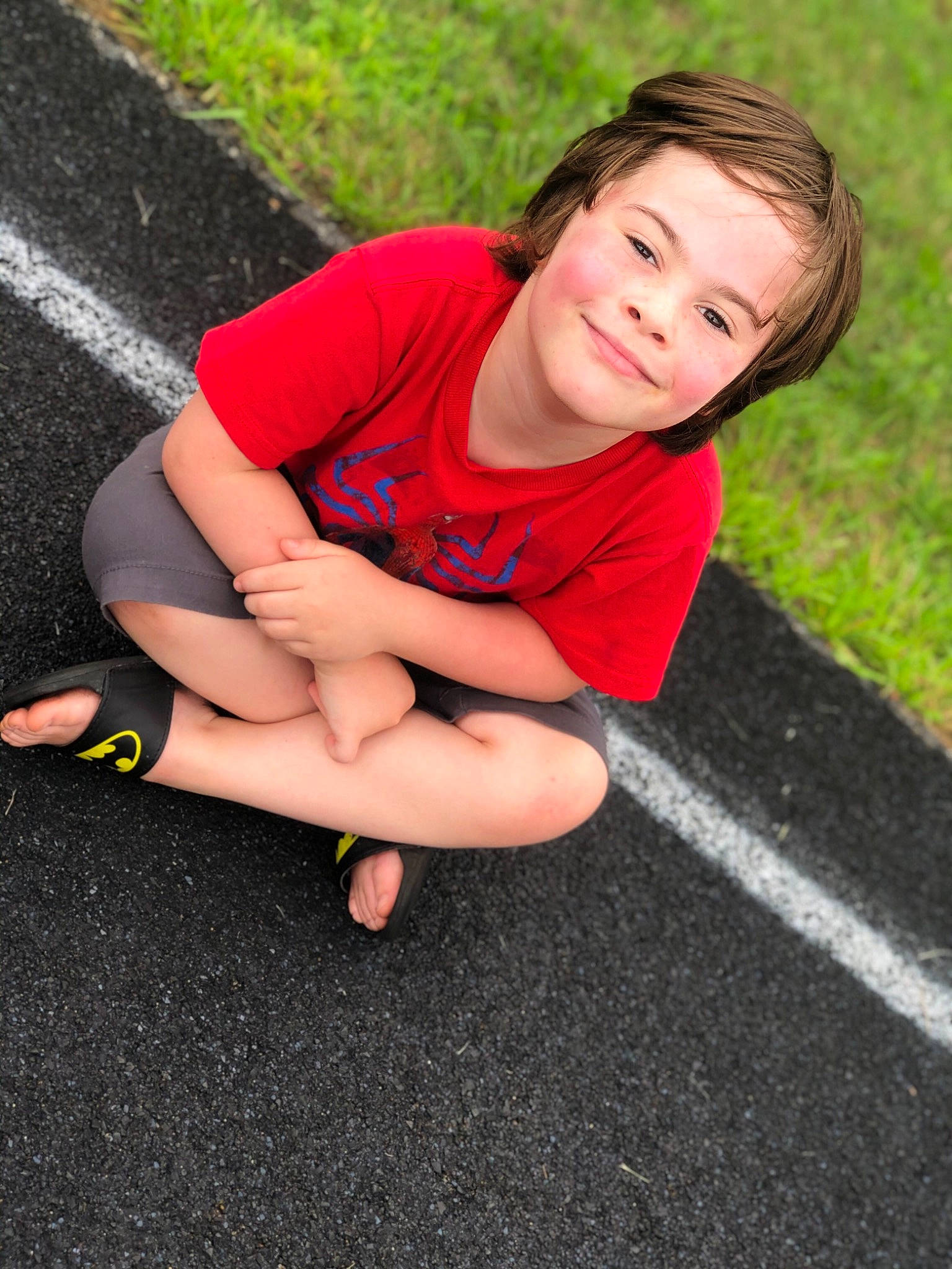 Jose is registered to the contest to win money with this photo: arm, asphalt, beauty, child, footwear, grass, hand, human_body, human_leg, joint, joy, knee, leg, person, photography, red, sitting, skin, smile, summer