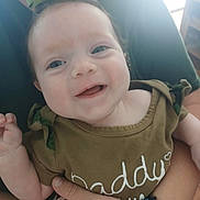 Mattalyn is registered to the contest to win money with this photo: baby, child, smiling, green_bow, green_clothing, adult_hand, wristband, indoor, portrait, face, happy, infant, close_up, person, casual, holding, cute, young_child, apparel, human