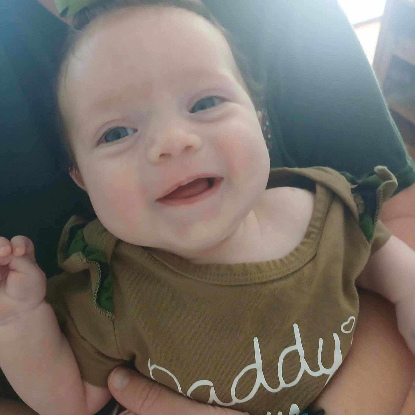 Mattalyn is registered to the contest to win money with this photo: adult_hand, apparel, baby, casual, child, close_up, cute, face, green_bow, green_clothing, happy, holding, human, indoor, infant, person, portrait, smiling, wristband, young_child