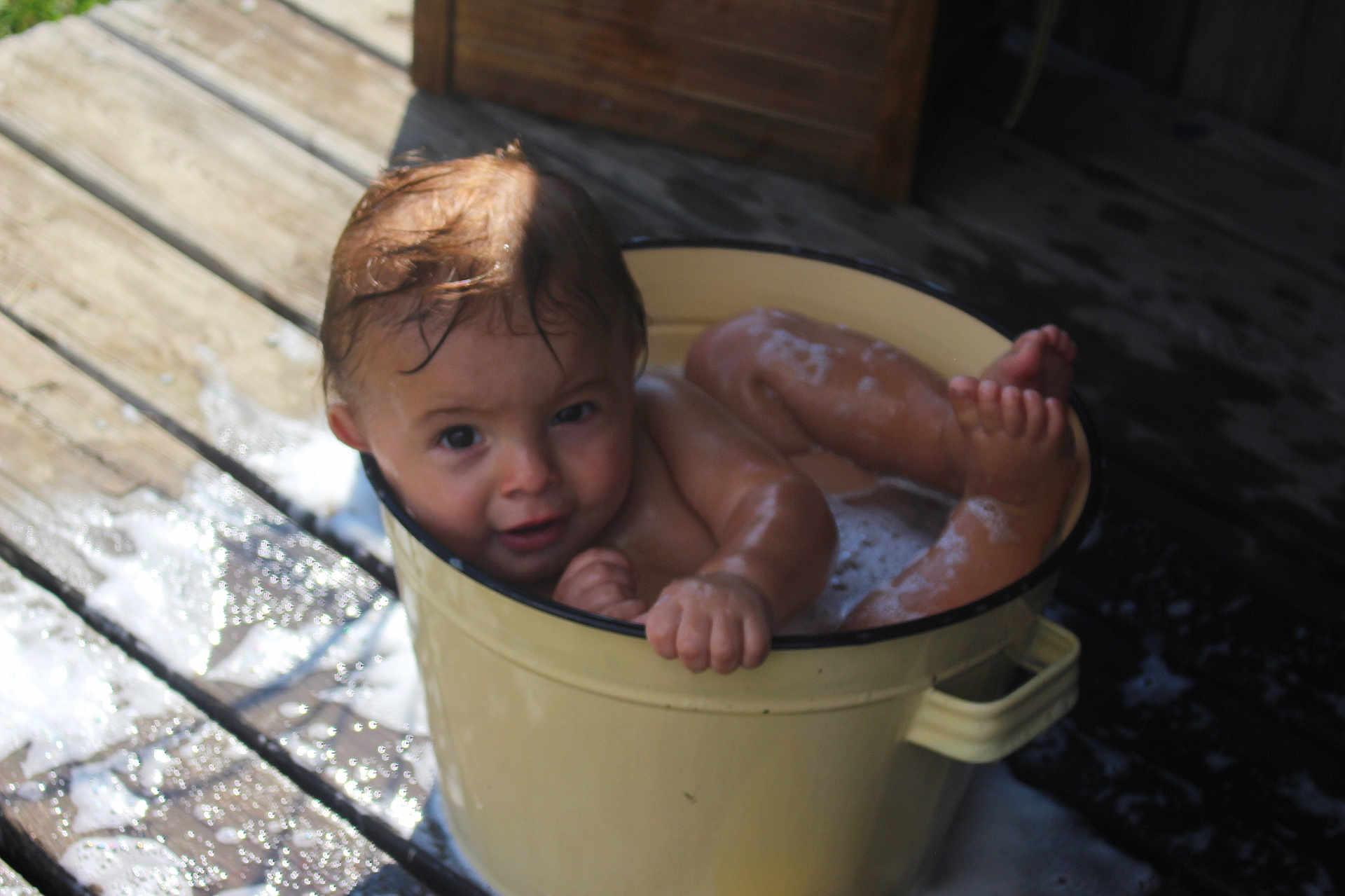 Easton is registered to the contest to win money with this photo: toddler, child, bucket, bath, soap, bubbles, water, wet, wooden_deck, outdoor, playful, curious, baby, skin, face, head, legs, feet, hands, expression