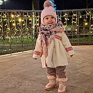 Alexia participe au concours pour gagner de l'argent avec cette photo : toddler, child, winter_clothing, hat, scarf, boots, outdoor, night, lights, fairy_lights, pole, fence, curious, smile, cold_weather, park, concrete_floor, cute, fashion, cozy