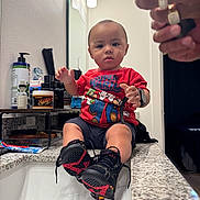 Wes is registered to the contest to win money with this photo: toddler, child, bathroom, sink, countertop, super_mario, red_shirt, black_shoes, sneakers, smartwatch, mirror, hands, rings, toiletries, toothpaste, soap, bottle, person, indoor, casual