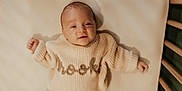 Brooks is registered to the contest to win money with this photo: baby, infant, child, smiling, knit_sweater, beige, soft_light, crib, wooden_rail, portrait, laying_down, cute, warm_tones, closeup, cozy, sleeve, happy, face, fingers, indoors