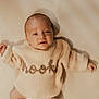 baby, infant, child, smiling, knit_sweater, beige, soft_light, crib, wooden_rail, portrait, laying_down, cute, warm_tones, closeup, cozy, sleeve, happy, face, fingers, indoors