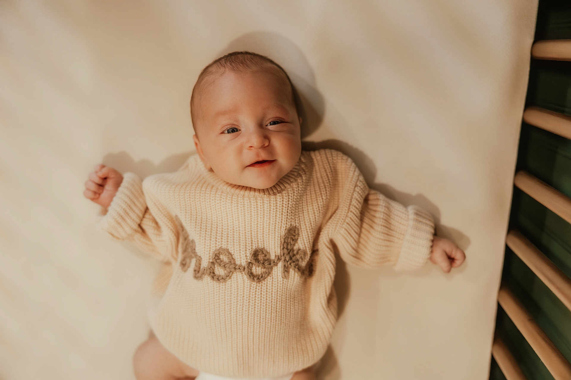 Brooks is registered to the contest to win money with this photo: baby, infant, child, smiling, knit_sweater, beige, soft_light, crib, wooden_rail, portrait, laying_down, cute, warm_tones, closeup, cozy, sleeve, happy, face, fingers, indoors