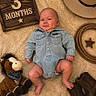 Henry is registered to the contest to win money with this photo: baby, denim_shirt, plush_toy, cowboy_hat, rope, boots, wooden_sign, milestone, smile, blanket, infant, cute, portrait, indoors, soft_texture, child, cowboy_theme, sitting, face, person