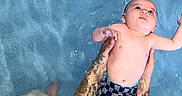 Jeremy is registered to the contest to win money with this photo: baby, child, swimming_pool, water, tattoos, arms, holding, checkered_shorts, floating, skin, summer, playful, young, swimwear, recreation, person, outdoor, blue, refreshing, fun