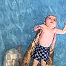 baby, child, swimming_pool, water, tattoos, arms, holding, checkered_shorts, floating, skin, summer, playful, young, swimwear, recreation, person, outdoor, blue, refreshing, fun