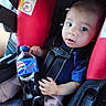 baby, child, car_seat, seatbelt, pepsi_bottle, drink, red_padding, blue_shirt, infant, portrait, indoor, seat, holding, wide_eyes, curious, person, young_child, casual_clothing, sitting, bottle