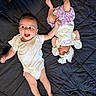 baby, infant, child, smiling, sleeping, hand_holding, blanket, headband, mittens, onesie, purple_skirt, quilted_bedspread, cute, adorable, lying_down, indoors, happy, peaceful, two_children, sibling