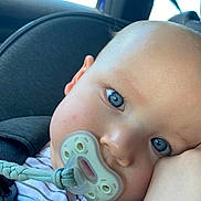 Noah is registered to the contest to win money with this photo: baby, pacifier, car_seat, blue_eyes, close_up, child, infant, face, skin, seatbelt, stripes, comfort, cute, young_child, indoors, resting, head, expression, soft_light, person