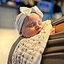 baby, sleeping, headband, bow, blanket, patterned_blanket, infant, closeup, peaceful, soft_lighting, portrait, child, person, indoor, cozy, resting, human, cute, wrapped, toddler