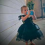 Rosalie is registered to the contest to win money with this photo: toddler, child, dress, black_dress, barefoot, indoor, wooden_wall, plant, blue_cup, drinking, person, curious, floor, home, young_child, sleeves, short_hair, standing, casual, portrait