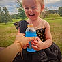 Rosalie joined the competition — help win amazing prizes! child, toddler, smiling, dress, sparkly, black_dress, blue_drink, bottle, hand, outdoor, grass, trees, happy, laughing, person, nature, daylight, fun, cute, joy