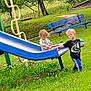 Ezra-lya is registered to the contest to win money with this photo: toddler, child, slide, playground, grass, bench, pacifier, sippy_cup, outdoor, greenery, tree, play, fun, summer, casual_clothing, blue, yellow, young_child, nature, park