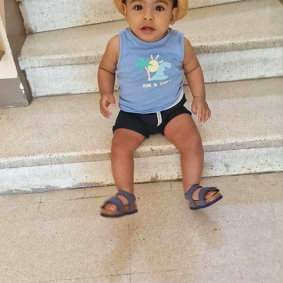 Raheem participe au concours pour gagner de l'argent avec cette photo : bare_arms, blue_shirt, casual_clothing, child, concrete, curious, cute, expression, floor, hat, indoor, looking_up, person, portrait, sandals, shorts, sitting, stairs, toddler, young_child