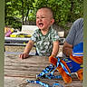 Zaid joined the competition — help win amazing prizes! adult_arm, casual_clothing, child, crying, daytime, expression, fence, greenery, leash, nature, outdoor, person, picnic_table, playtime, plush_toy, summer, toddler, toy, trees, wood