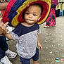 Raphaël a rejoint le concours — aidez-le/la à gagner de superbes lots ! adult, background, barefoot, casual_clothing, celebration, child, concrete_floor, confetti, dress, expression, footwear, hand_holding, hat, outdoor, party, people, sneakers, sombrero, striped_shirt, toddler