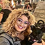 woman, glasses, curly_hair, smile, dog, pet, holding, portrait, outdoor, night, bonfire, people, crowd, trailer, wooden_steps, chair, bracelet, event, hairstyle, happy