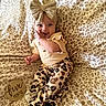 baby, infant, child, smiling, leopard_print, headband, bow, clothing, pants, blanket, plaid, milestone, wooden_plaque, sitting, cute, happy, portrait, indoors, person, fashion