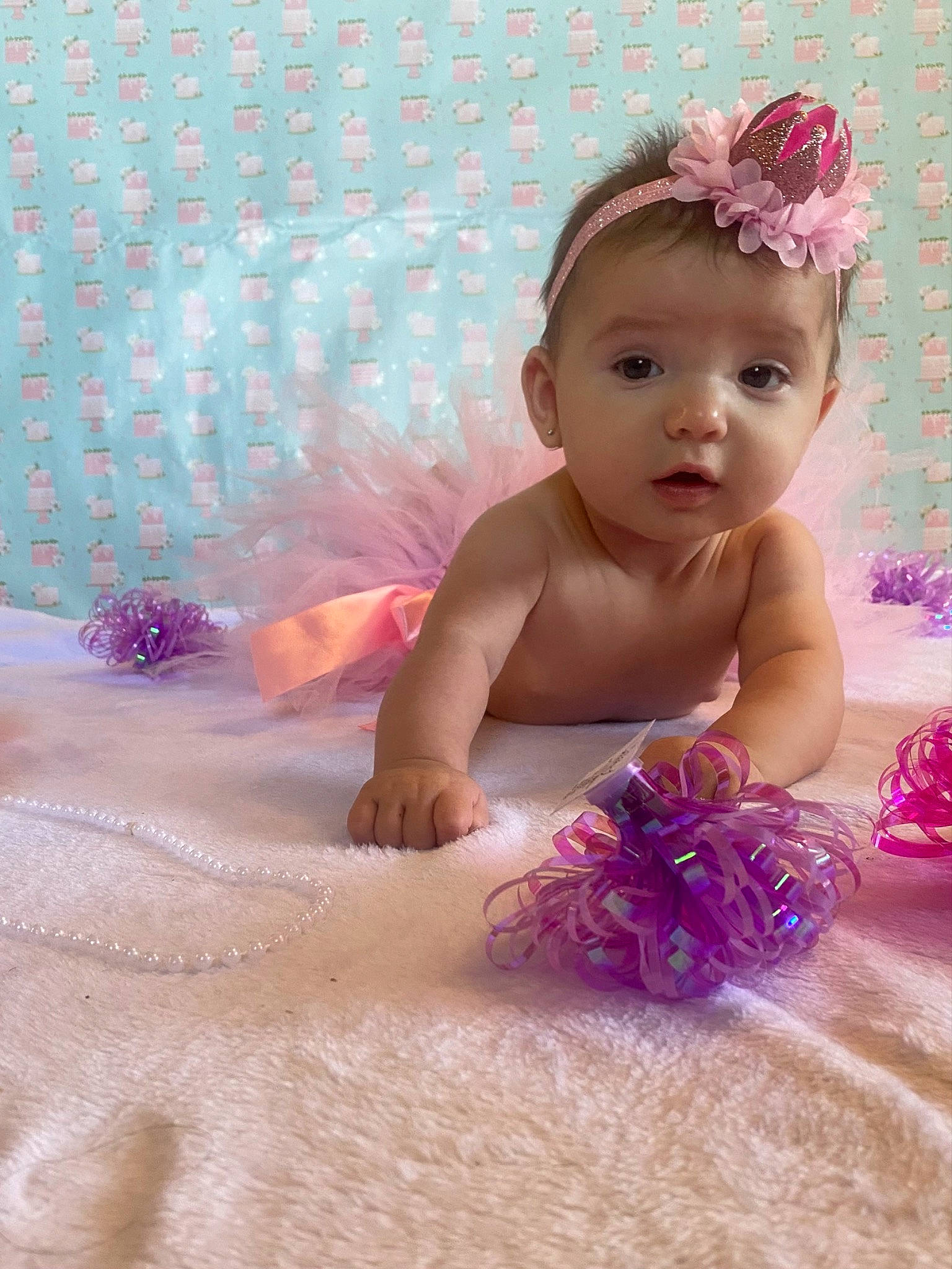Maylee is registered to the contest to win money with this photo: baby, baby_toddler_clothing, bathing, child, comfort, fashion_accessory, finger, fun, happy, headpiece, linens, magenta, person, petal, pink, product, purple, sand, skin, textile
